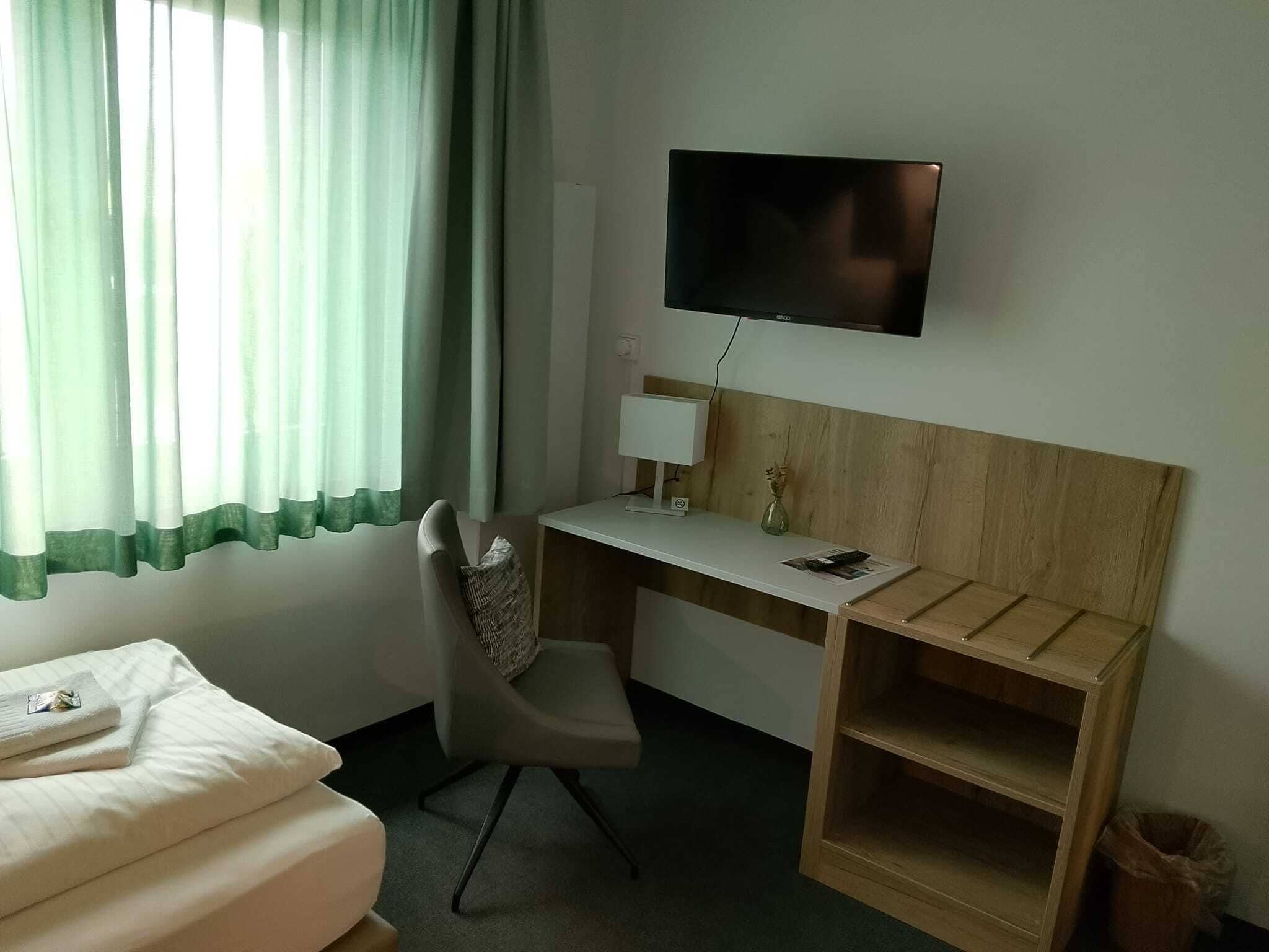 A hotel room with a bed, a desk with a computer monitor, a chair, and a TV mounted on the wall.