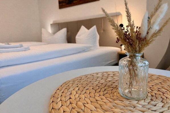 Ein Hotelzimmer mit Bett, einem Nachttisch mit einer Vase getrockneter Pflanzen und einer gewebten Unterlage.