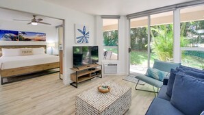 Un dormitorio moderno con cama, televisor y balcón con vistas a zonas verdes.