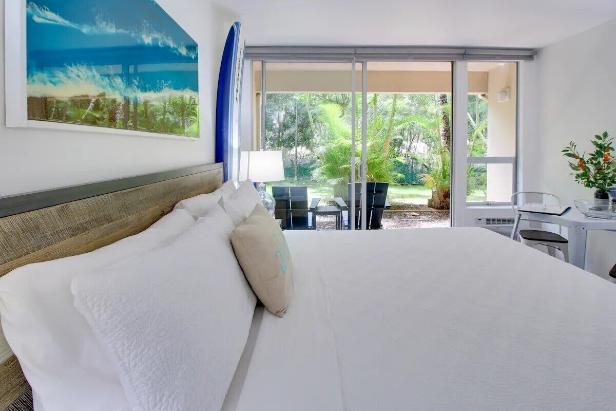 Une chambre d’hôtel avec un grand lit, un bureau avec une chaise et une vue sur un jardin, accessible par une porte-fenêtre coulissante.