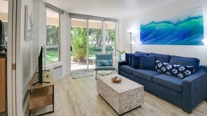 A modern living room with a blue sofa, a coffee table, and a large window with a view of greenery.