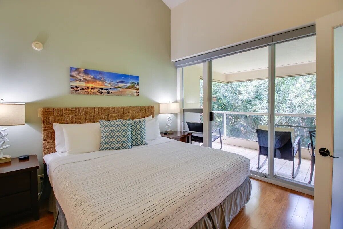 A bedroom with a large bed, a painting on the wall, and a balcony with chairs.