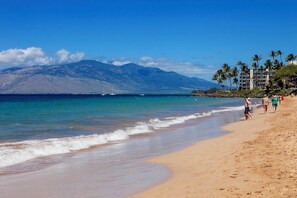 Una playa con agua azul cristalina, una orilla arenosa y una montaña al fondo.