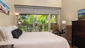 Habitación de hotel con una cama grande, vistas a vegetación exuberante, un televisor y una silla de mimbre.