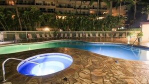Una piscina con hidromasaje, rodeada de palmeras y una valla blanca.
