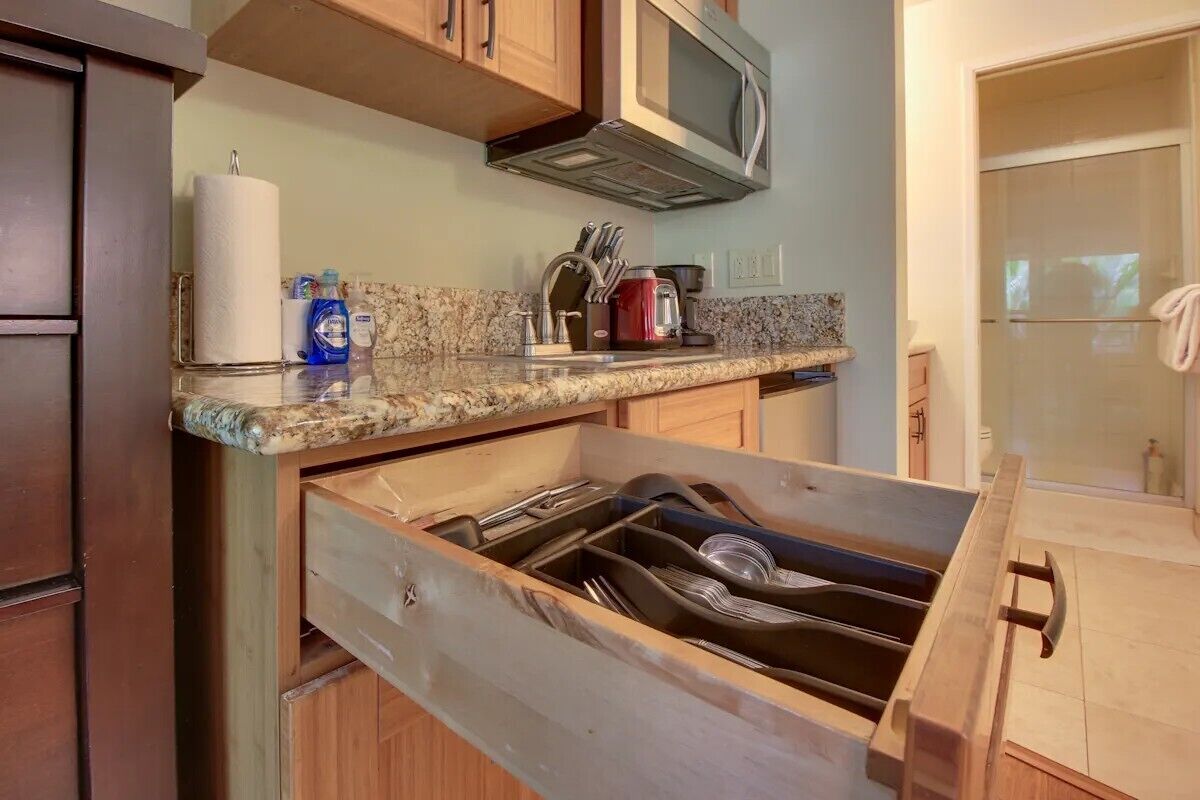 A kitchen with wooden cabinets, a granite countertop, a microwave, and a dish rack.