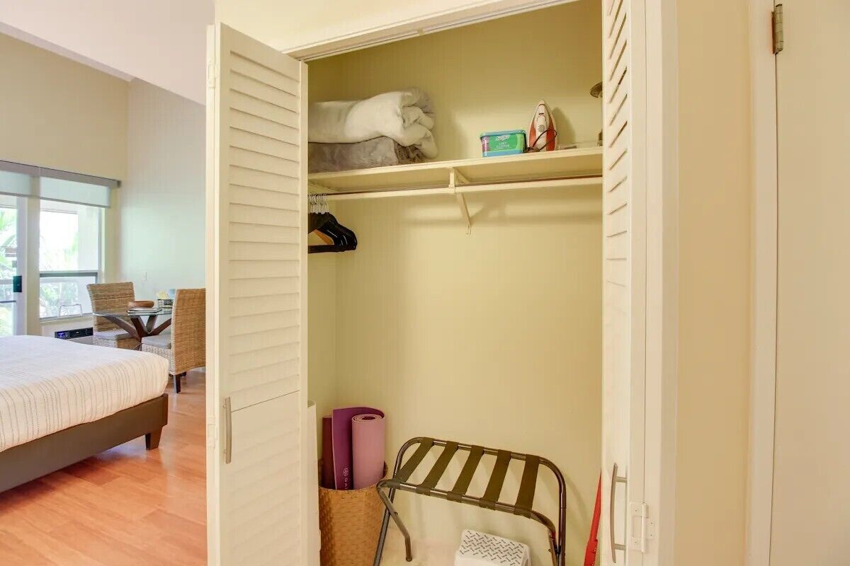 Un dormitorio con una cama, una silla, una mesa y un armario con repisas y espacio para colgar.