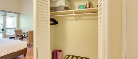 Un dormitorio con una cama, una silla, una mesa y un armario con repisas y espacio para colgar.