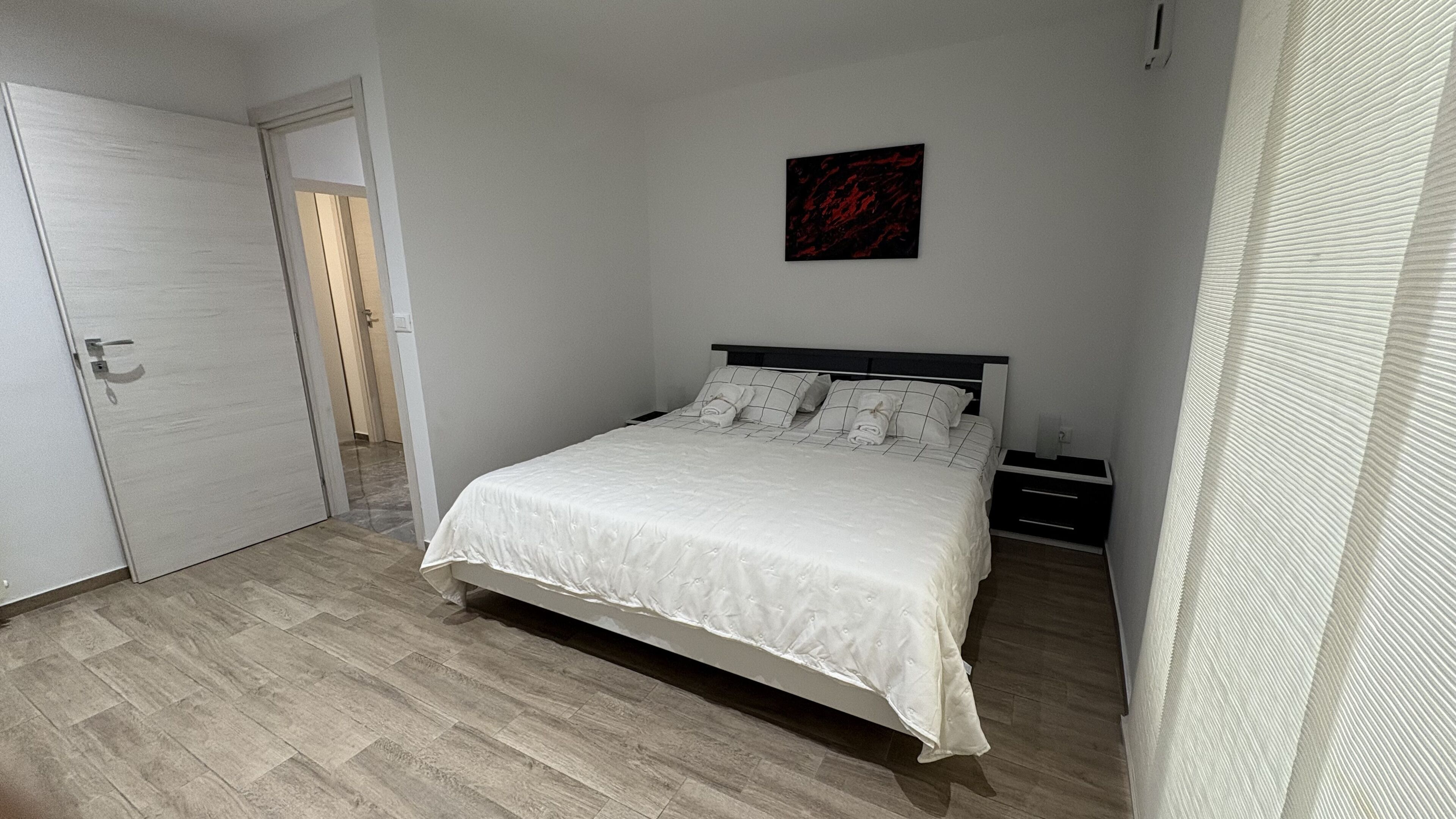A bedroom with a bed, a nightstand, a door, and a wall-mounted artwork.