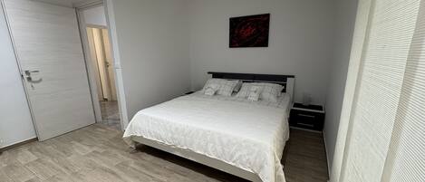 A bedroom with a bed, a nightstand, a door, and a wall-mounted artwork.