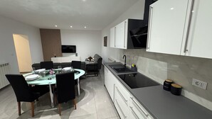 Una cucina moderna con mobili bianchi, un piano di lavoro nero e un'area pranzo con un tavolo e sedie in vetro.