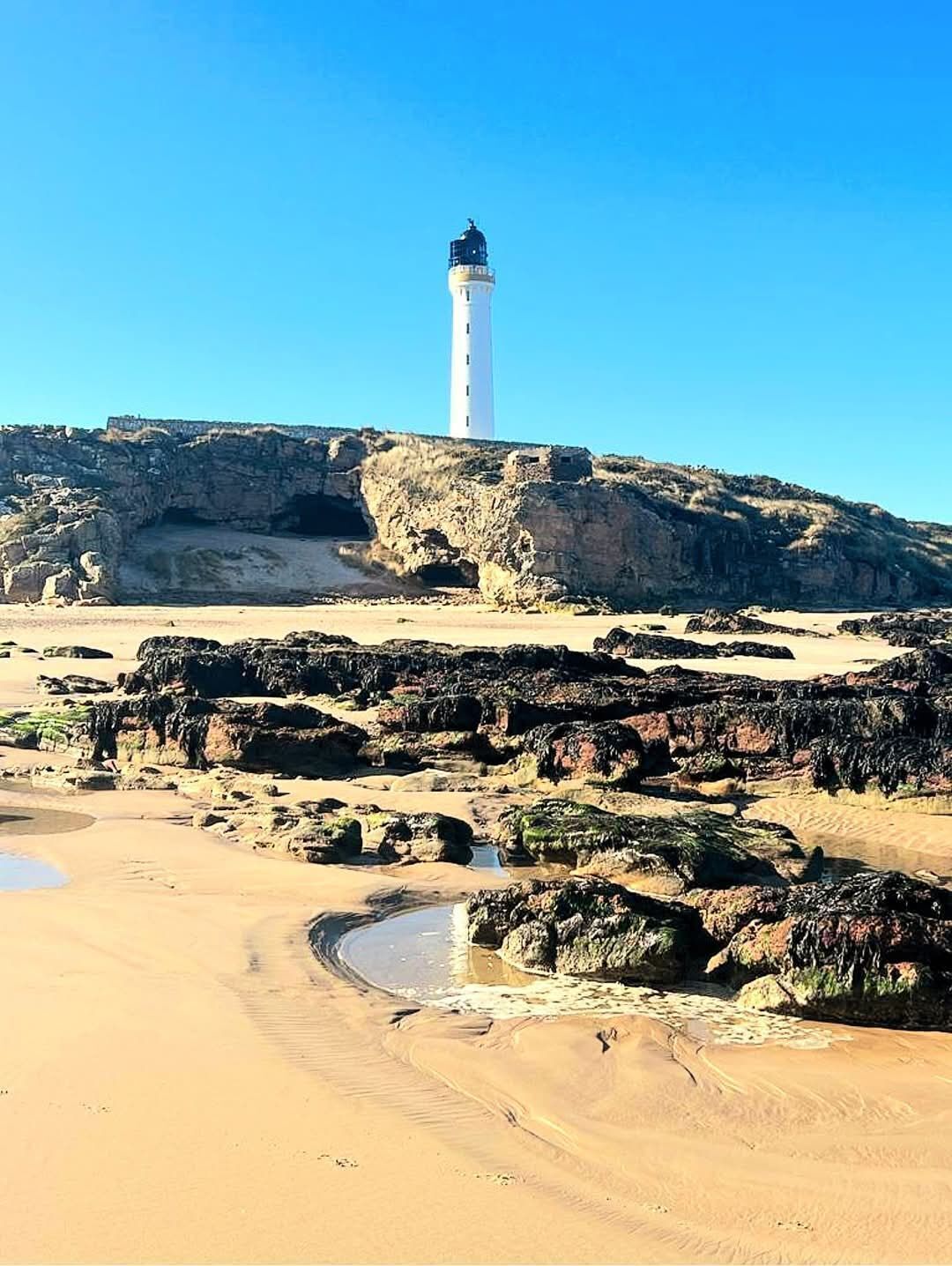 Un faro sobre un promontorio rocoso con un cielo azul despejado.