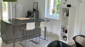 Et moderne køkken med en central ø, barstole, kaffemaskine og en hvid reol.