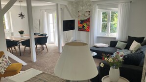 En moderne stue med spiseplads, en sofa, et fjernsyn og et stort vindue med gardiner.