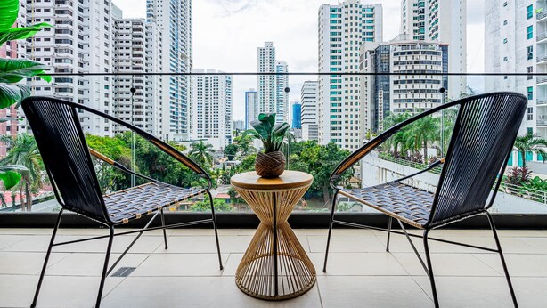 A balcony with two black wicker chairs and a small round table with a pineapple centerpiece.
