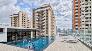 A rooftop pool area with a clear view of the city skyline, modern buildings, and a glass railing.