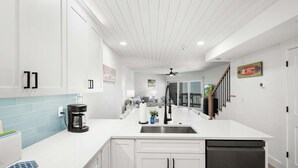 Una cocina moderna con armarios blancos, una isla grande con pileta y un ventilador de techo.