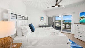 Habitación de hotel con cama, escritorio, televisor y balcón con vista al océano.