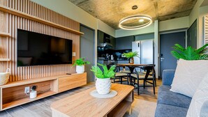 Una sala moderna con un televisor de pantalla plana grande, paneles de madera, un comedor con mesa y sillas, y un sofá gris.