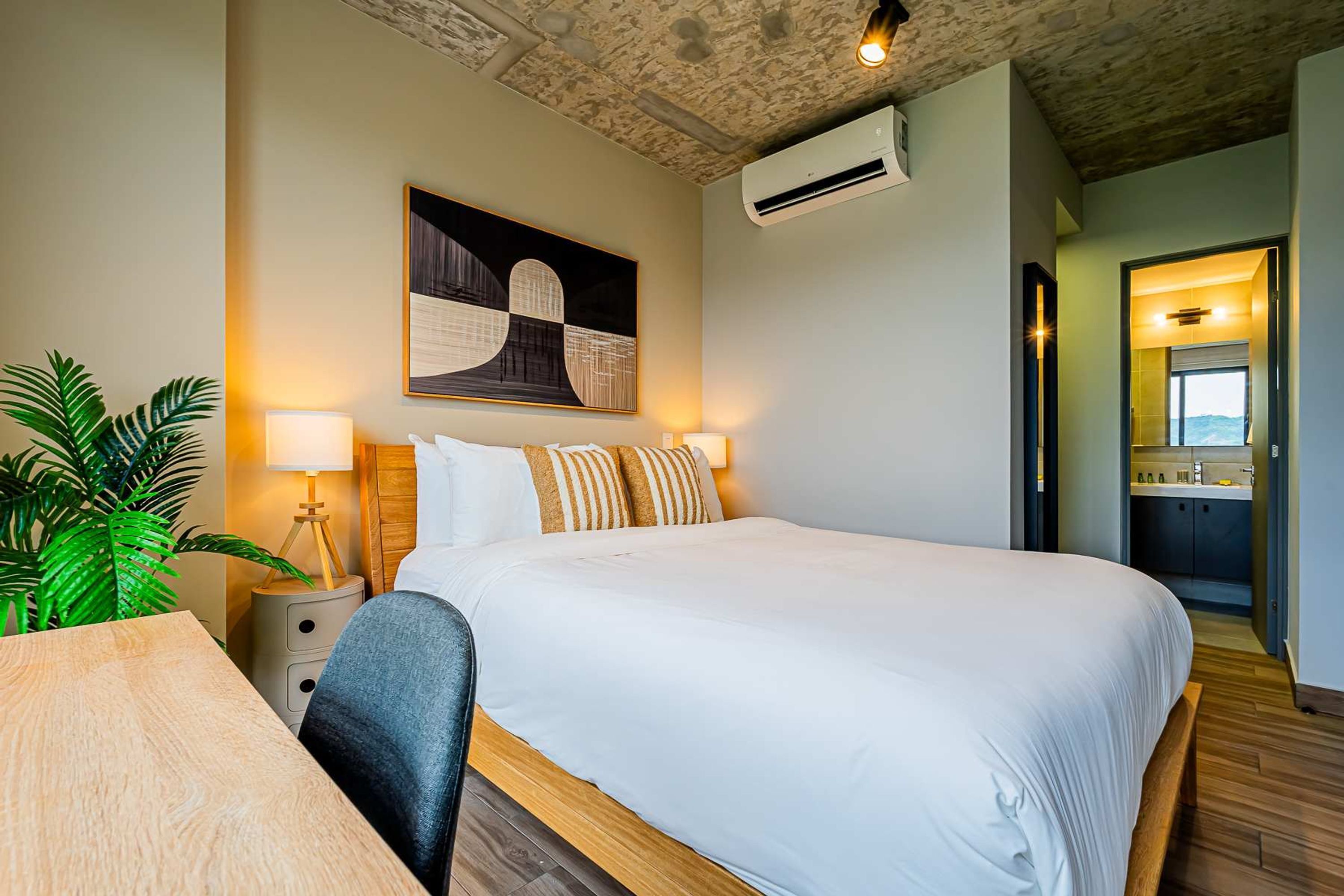 Ein ordentlich eingerichtetes Hotelzimmer mit einem großen Bett, Nachttischlampen, einem Schreibtisch und einem Blumentopf.