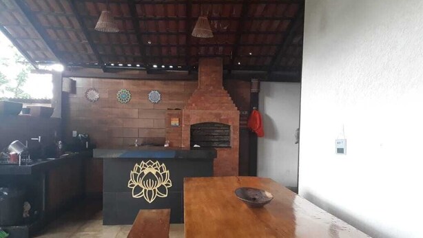 An outdoor kitchen area with a brick oven, wooden tables, and a decorative emblem on the counter. - Botanical Garden House, Tororó Waterfall (Brasília)