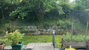 Een houten terras dat uitkomt op een tuin met potplanten en een bakstenen muur.