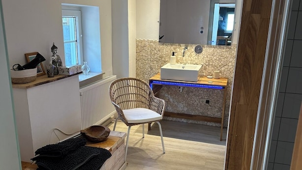 Een moderne badkamer met een backsplash van stenen mozaïek, een witte wastafel en een houten opbergmeubel.
