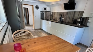 Een moderne keuken met witte kasten, een houten eettafel en rieten stoelen.