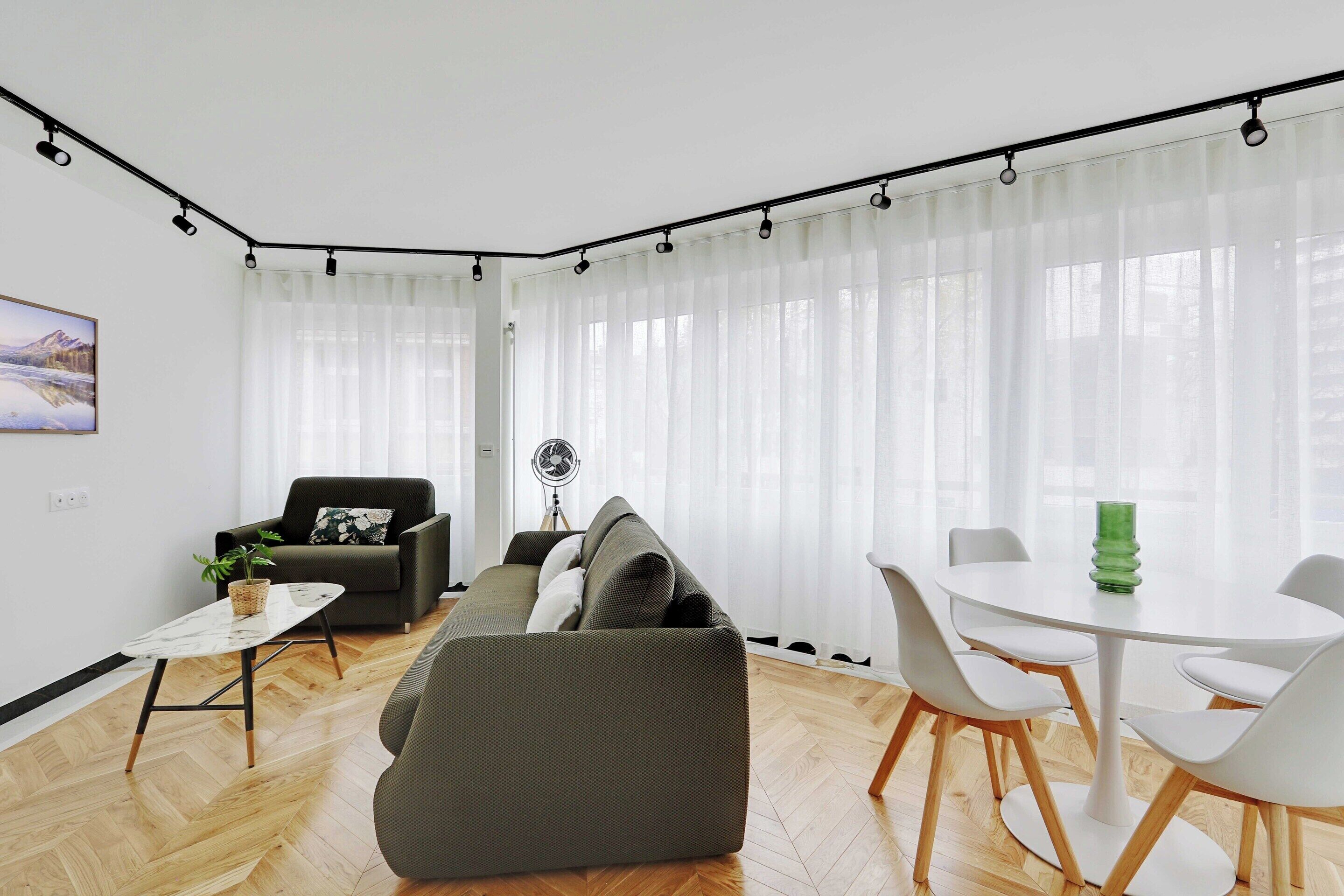 Un salon moderne avec un canapé, une table à manger et des chaises, ainsi qu’un ventilateur.