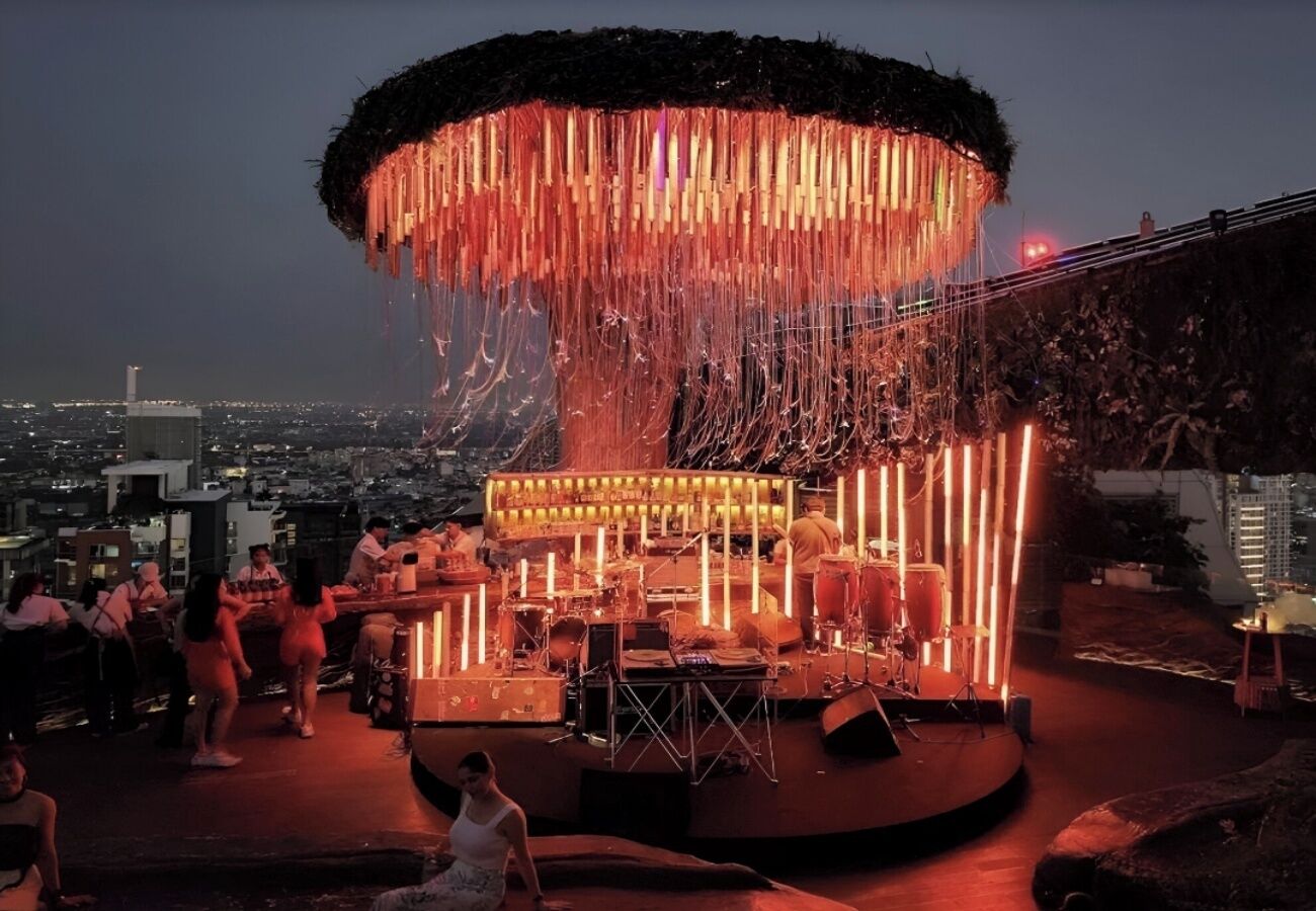A rooftop bar with a stage and seating area, overlooking a cityscape.