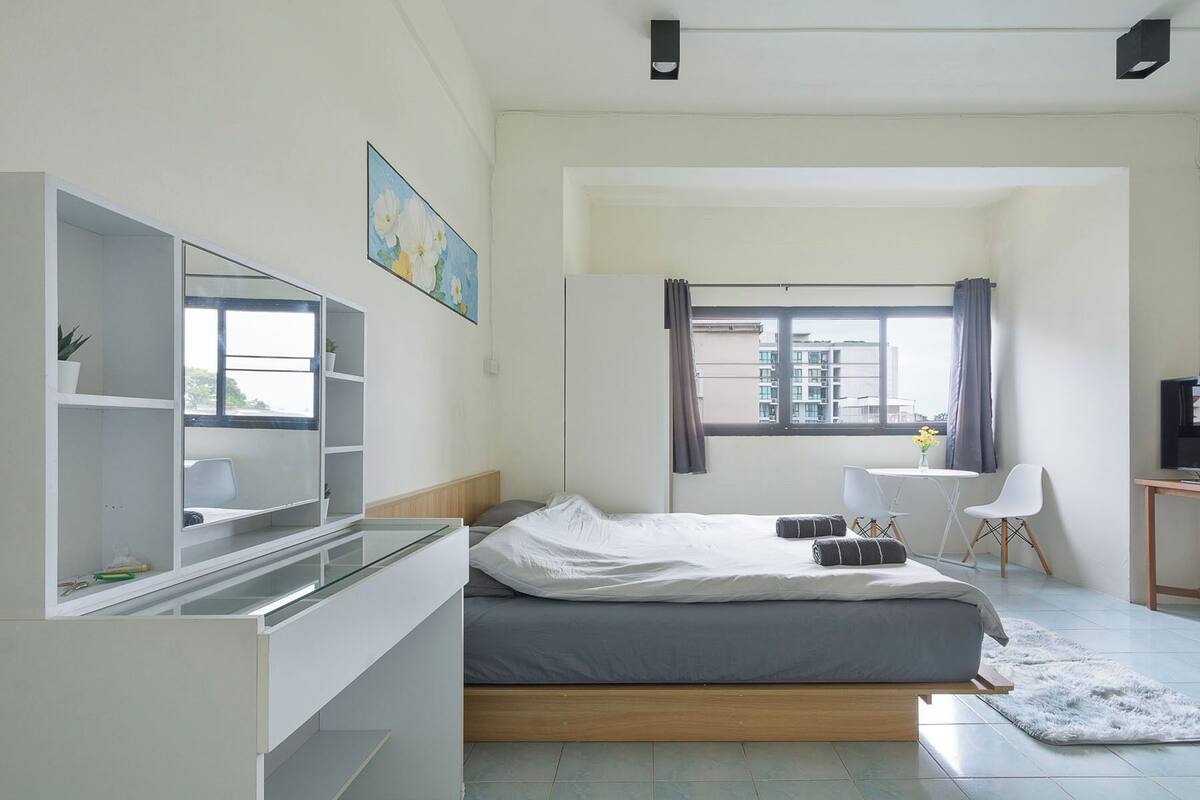 Een moderne slaapkamer met een bed, een bureau, een stoel, een raam en een schilderij aan de muur.