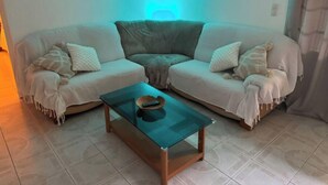 En stue med en tostrengers sofa, et sofabord i glas og et billede på væggen.