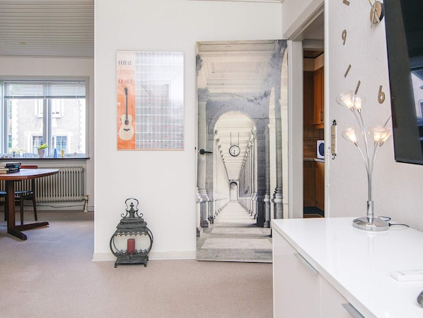 A room with a white desk, a framed guitar chords chart, a decorative metal stand, and a view of a hallway with a clock. - 6 Person Holiday Home in Ansager (Ansager)