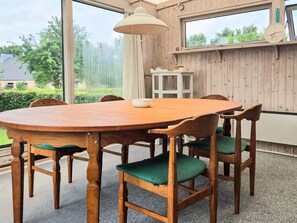 A round wooden dining table with chairs, a hanging light fixture, and a view of greenery outside. - 6 Person Holiday Home in Ansager (Ansager)