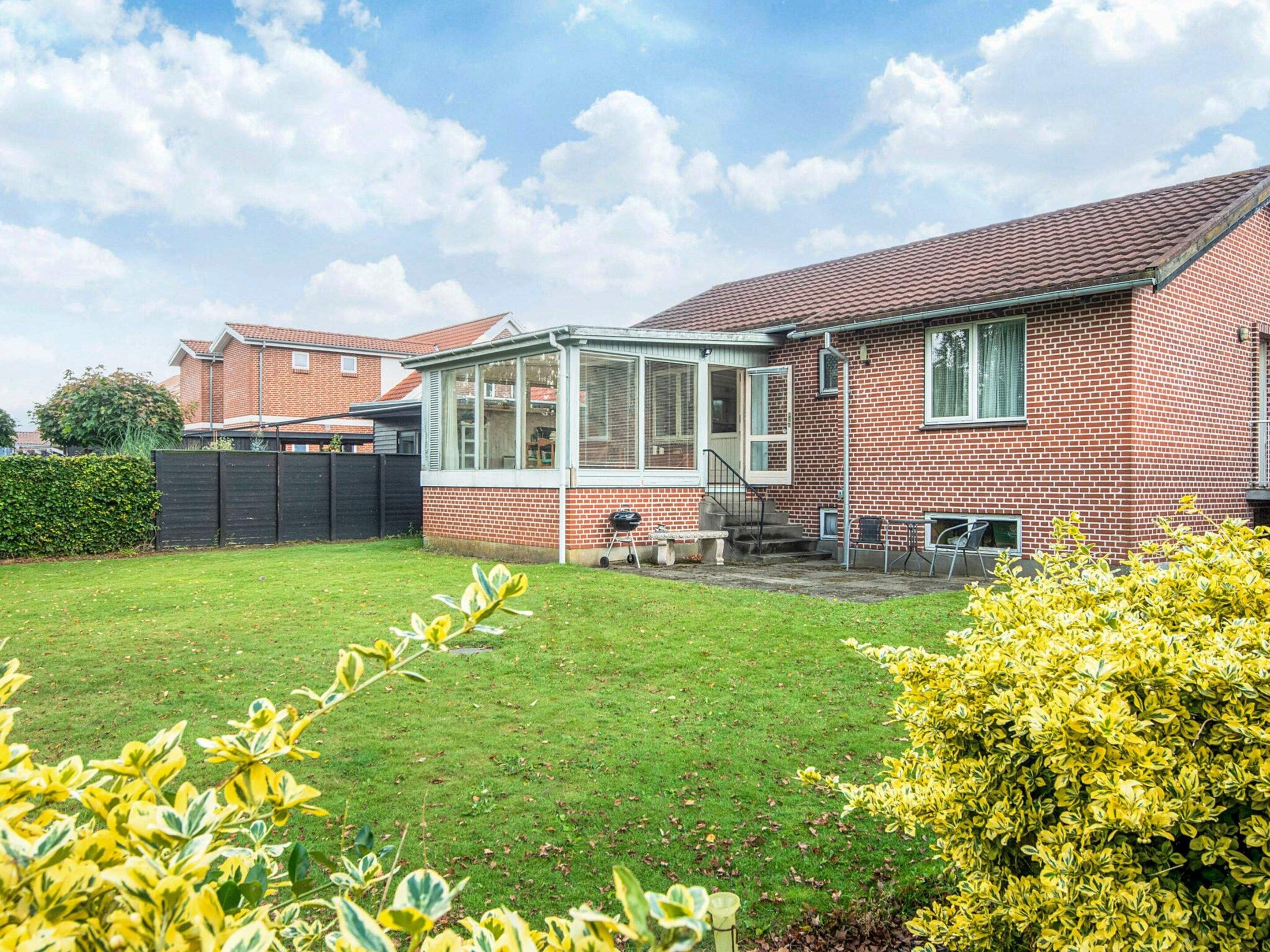 A residential house with a brick exterior, a conservatory, a lawn, and a garden with yellow foliage.