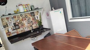 Een keuken met een houten tafel, een koelkast en een wandplank met diverse spullen.