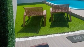 Een achtertuin met een zwembad, twee rieten stoelen en een kleine tuin.