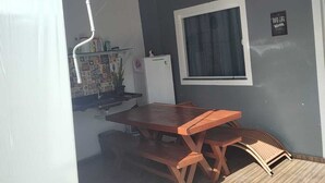 Een overdekt terras met een houten tafel en stoelen, een raam en een bord aan de muur.