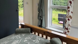 Un dormitorio con cama, ventana con vista a la vegetación y puerta que da al exterior.