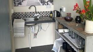 Una cocina compacta con un lavamanos, una estufa y una pequeña encimera. Hay una ventana con vistas a la vegetación exterior, y un cuadro en la pared.