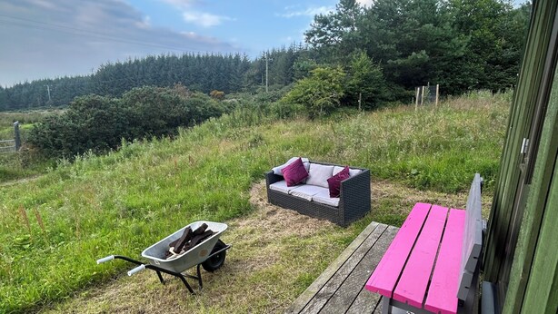 Una terraza de madera con una silla de mimbre, una mesita y una carretilla.