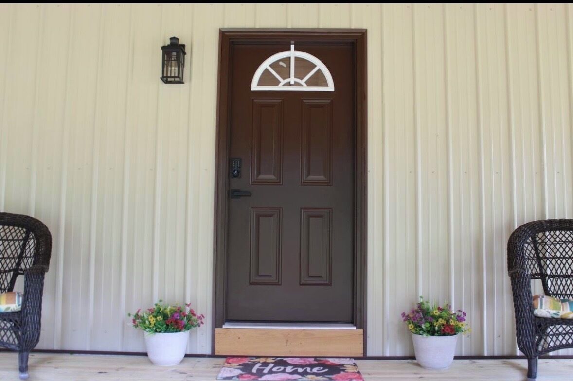 A brown door with a white decorative element above it, flanked by two wicker chairs with potted plants.