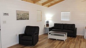 Un salon moderne avec un canapé en cuir noir, une table basse blanche et un tableau accroché au mur.