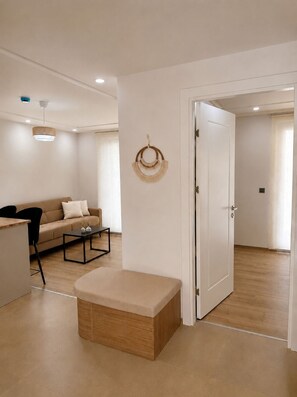A modern living room with a sofa, coffee table, ottoman, and a wall-mounted decorative item. - Oregano Side (Side)