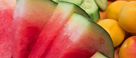 A wooden board with sliced watermelon, cucumbers, yellow cheese, and a few olives.