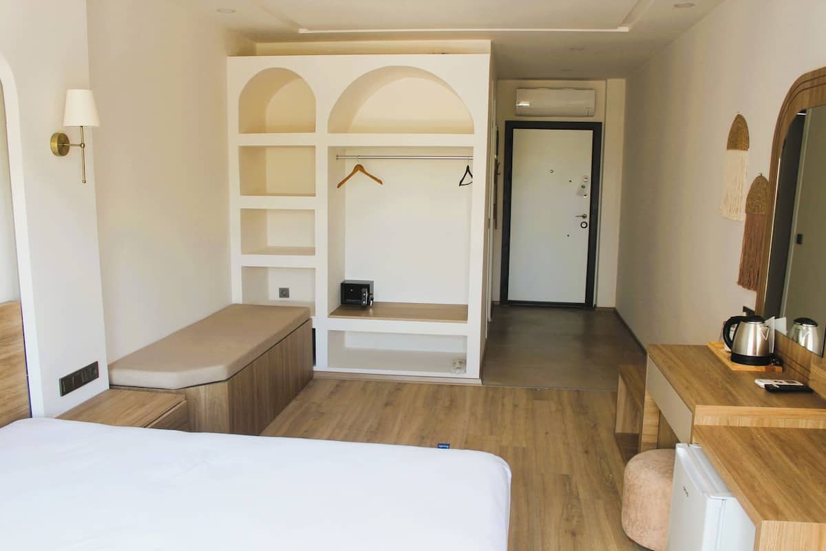 A hotel room with a bed, a wooden desk, a wardrobe with shelves, a hanging coat rack, and a mirror.