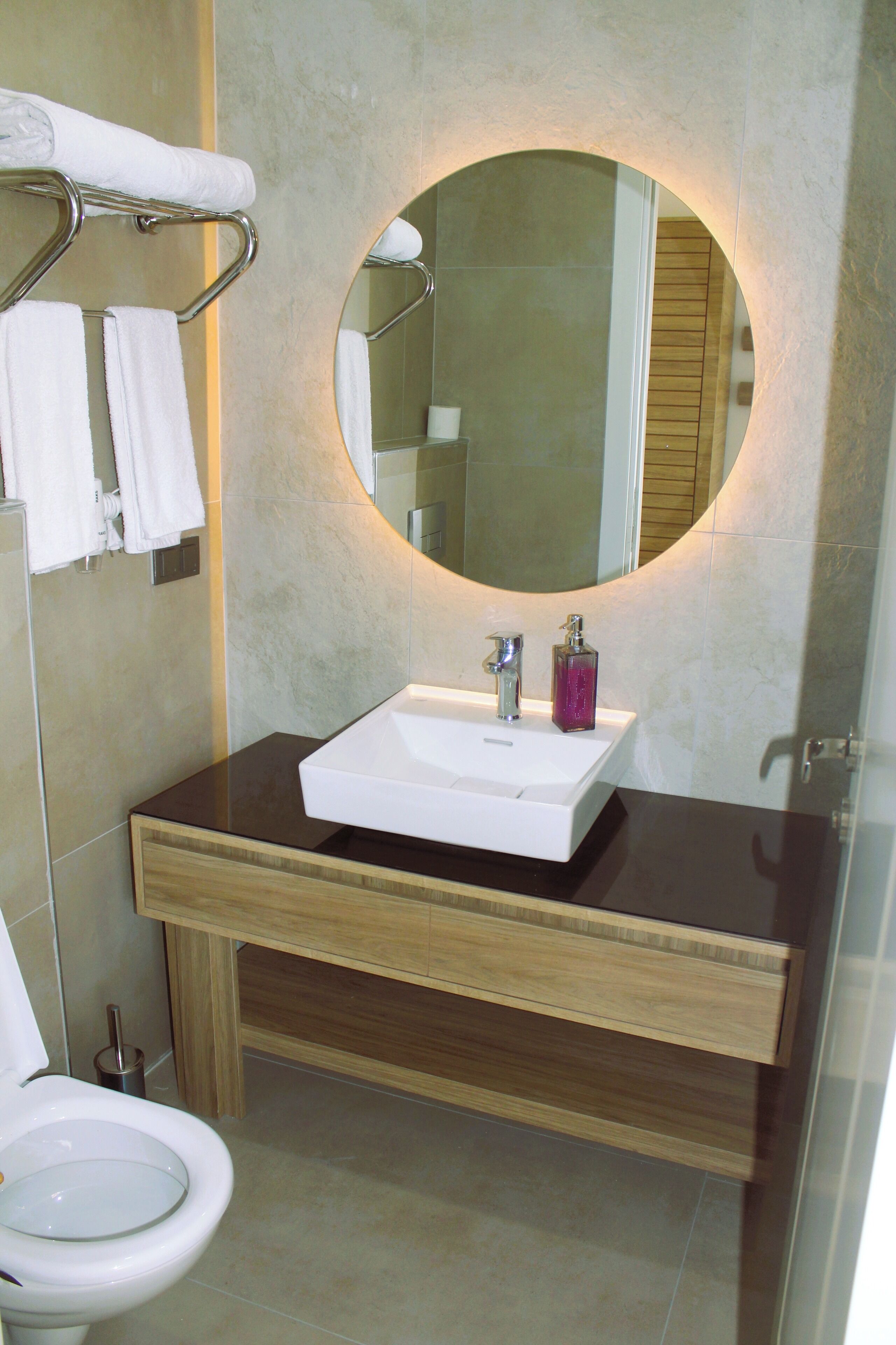 A modern bathroom with a white sink, a round mirror, and a toilet.
