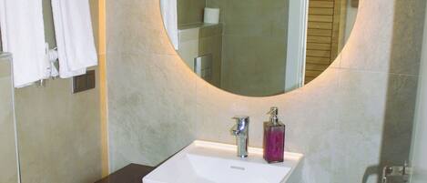A modern bathroom with a white sink, a round mirror, and a toilet.