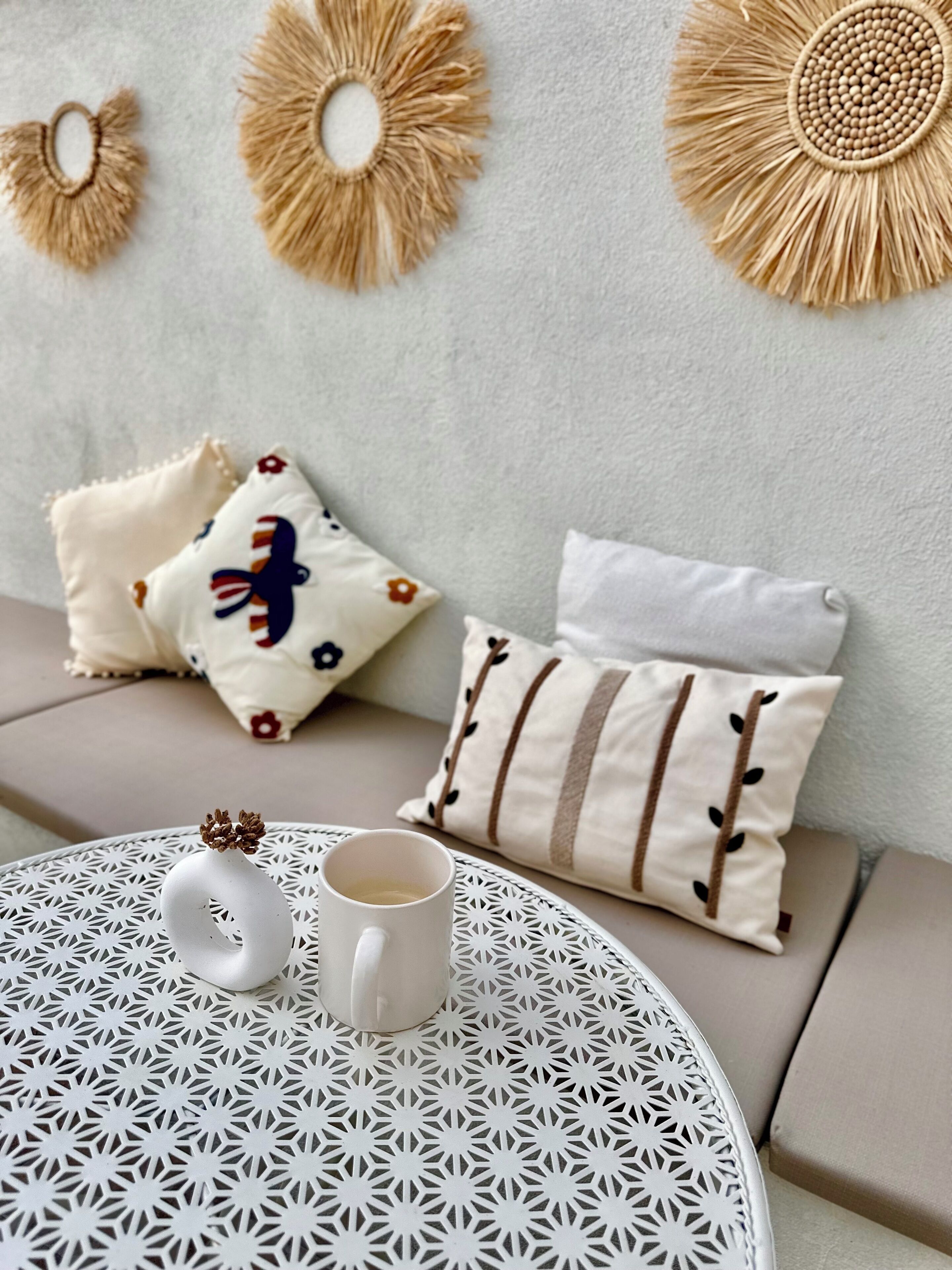 Ein runder Tisch mit einer weißen Tasse und einem dekorativen Gegenstand, ein Sofa mit gemusterten Kissen und Wandgestaltung.