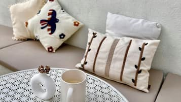 Ein runder Tisch mit einer weißen Tasse und einem dekorativen Gegenstand, ein Sofa mit gemusterten Kissen und Wandgestaltung.